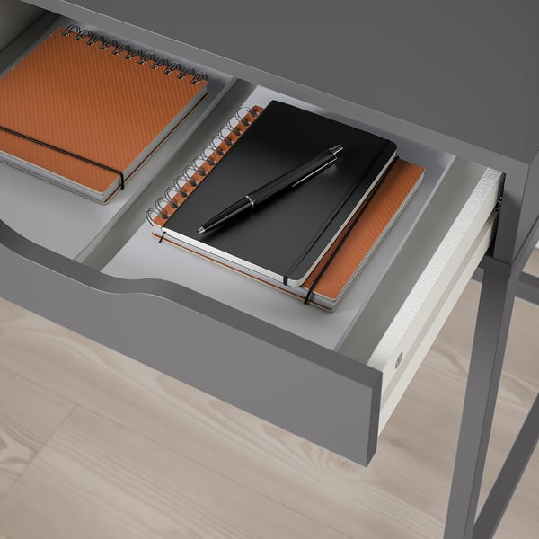 Open desk drawer with notebooks and pen, showcasing built-in storage.