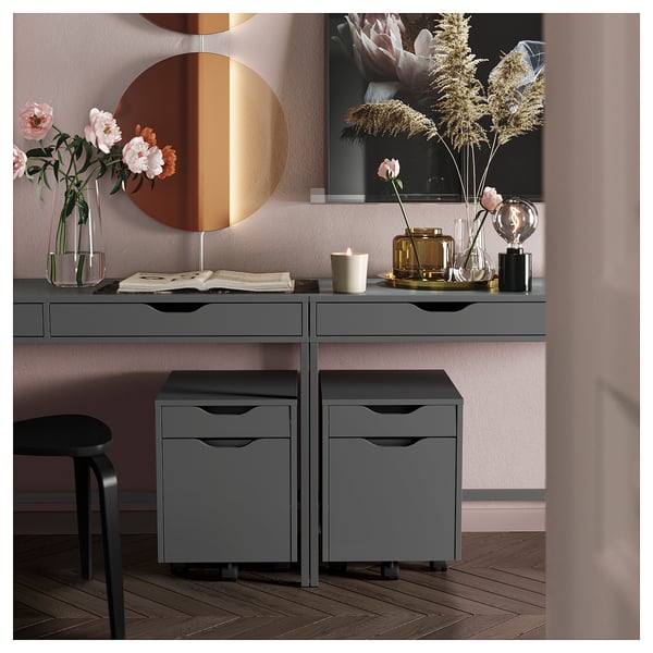 This image shows grey ALEX drawers with two drawer units, a round mirror, and decorative items on a desk with flowers and a candle.