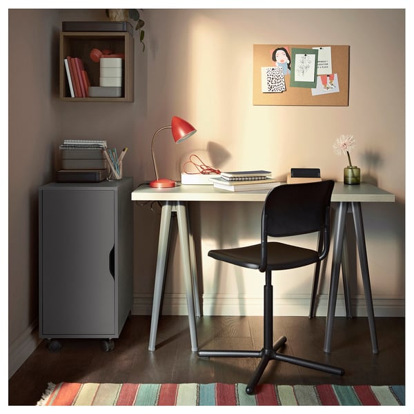 Home office with ALEX unit, desk, and adjustable chair. Red lamp, laptop, notes, and a flower.