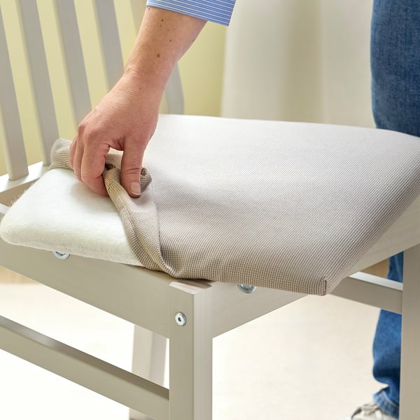 Person cleaning a chair with a white cushion and wooden frame, using a cloth.