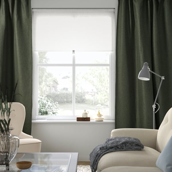 Modern living room with green curtains, white shade, and chair with throw.