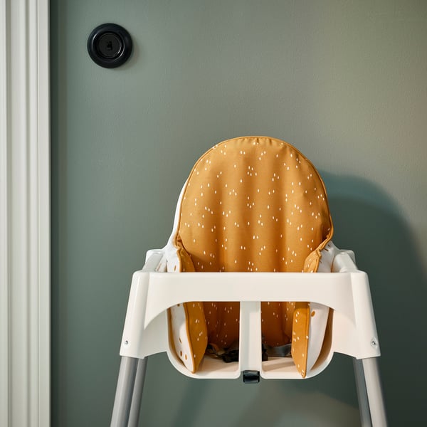 A white high chair with a yellow dotted cushion provides safe, comfortable support for young children during mealtime.