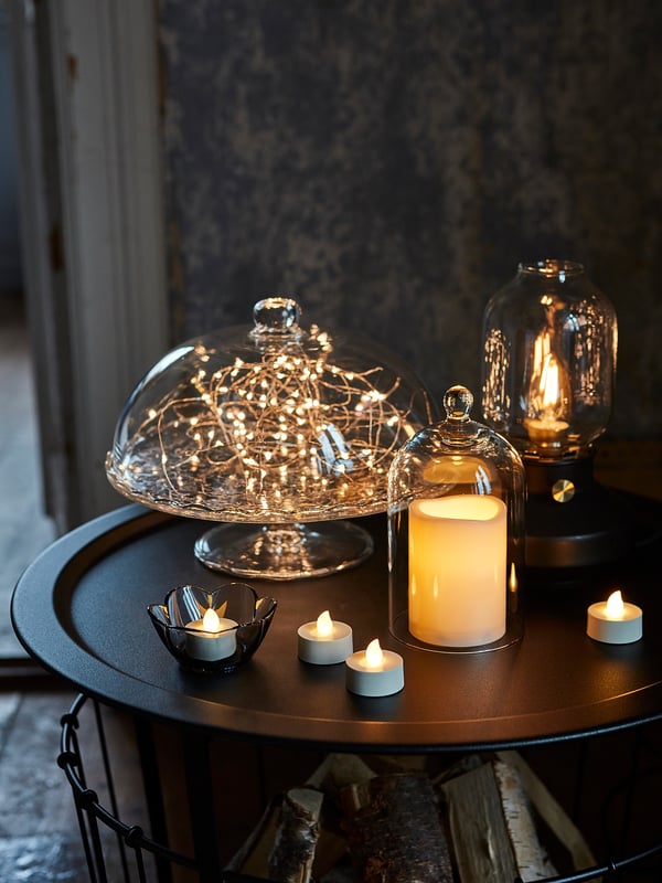 Clear glass cake dome with lights, round black tray, candles. Cosy, festive decor setup.