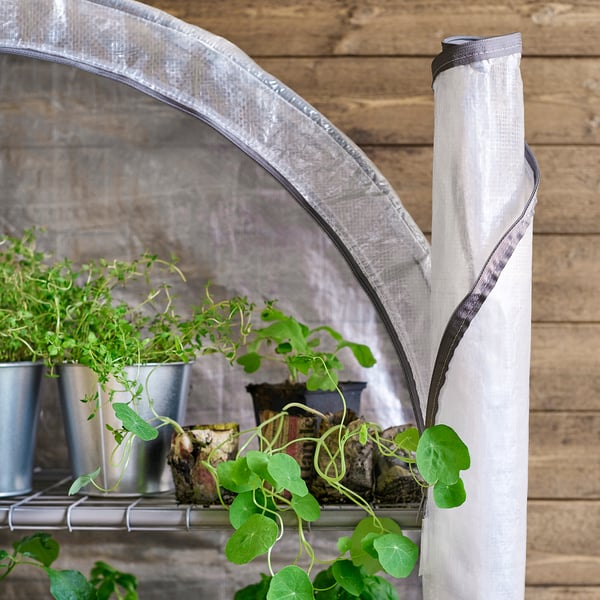 Small white ASPAREN greenhouse on a balcony with green plants inside.