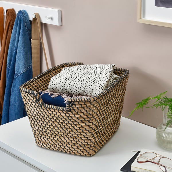 Basket on table holds folded clothes near wall hooks with coats.