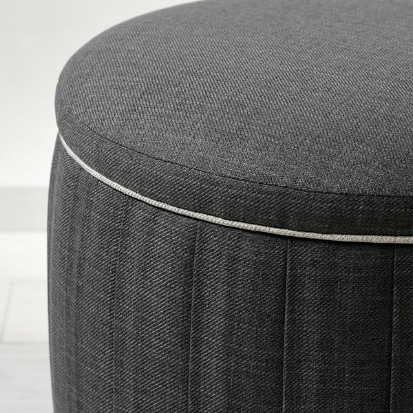 Round, dark grey upholstered footstool with stitched edges, showing quality fabric and design.