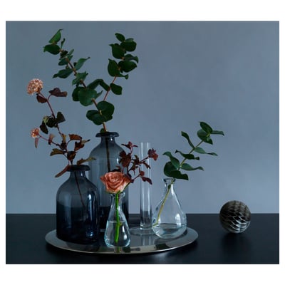 Simple still life with ÅTGÅNG blue, clear glass vases holding flowers on metal tray, grey background.