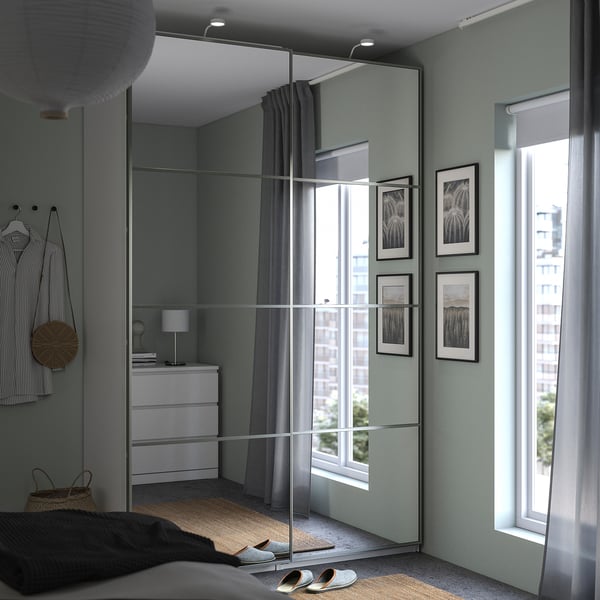 Modern bedroom with green walls, mirror closet, black-and-white photos, white dresser, bed with rug and slippers, sheer curtains.
