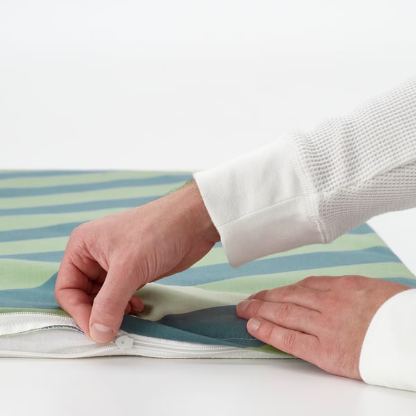 Person zipping a colourful, striped BÄNKKAMRAT seat pad, showcasing its removable cover for easy washing.