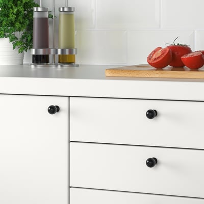 White kitchen drawers with black BAGGANÄS knobs. On counter, sliced tomatoes and oils.