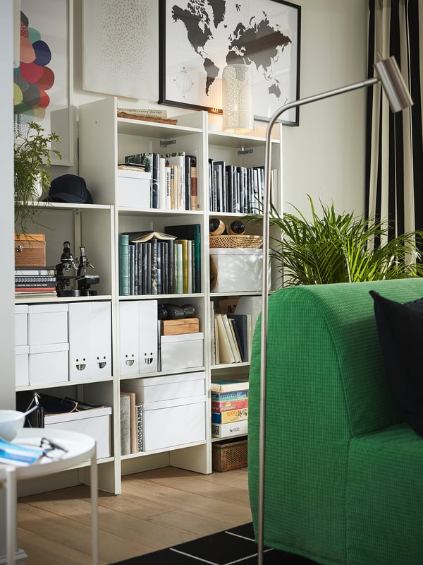 White bookshelf with books & decor, green armchair, plant.