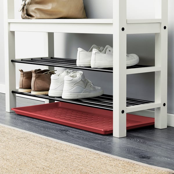 A red shoe mat placed under a shoe rack, protecting the floor from dirt and making cleaning easier.