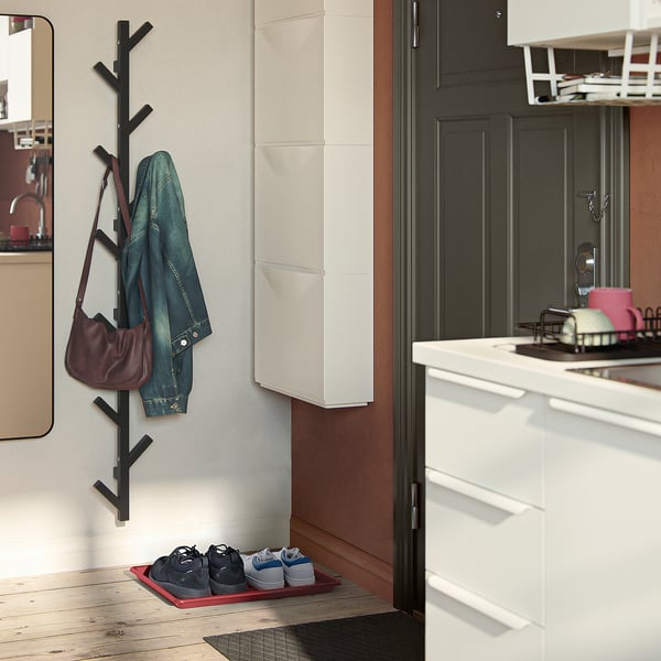 A hallway with a red BAGGMUCK mat, blue jacket, and maroon purse on black hooks, white cabinet.