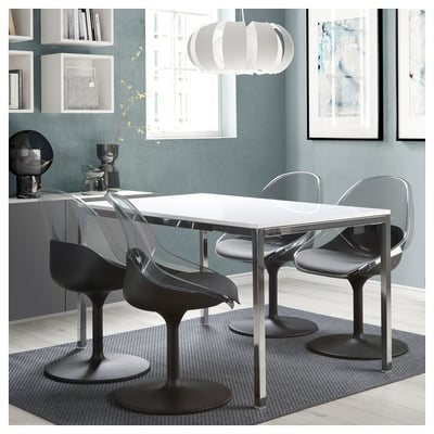 Modern dining set with white table and four black BALTSAR swivel chairs. Sleek, curved design, placed under a hanging light, against a teal wall.