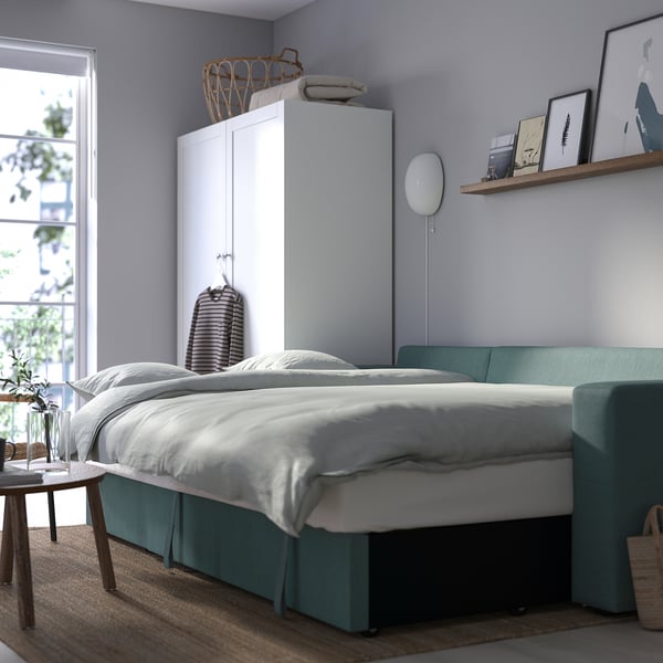 Cosy bedroom with green sofa-bed, white linens and wooden side table, offering comfort and practical storage.