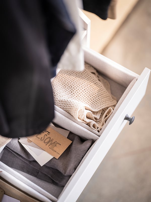 Open white drawer with neatly folded beige and grey linens, knitted blanket, and a folded note reading welcome 2022.