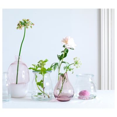 Five glass vases in pastel colours display flowers; arranged on a white table.
