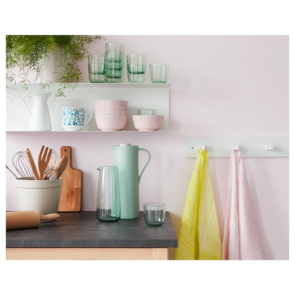 Kitchen counter with green glassware, pink bowls, wooden utensils, and yellow dish towels.