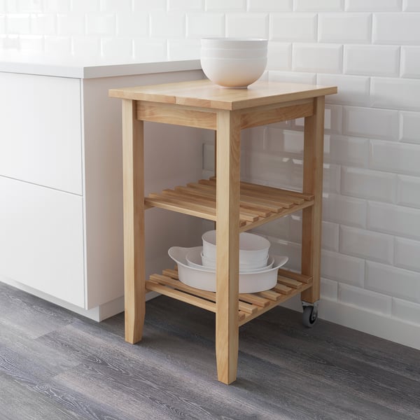 Light wooden kitchen cart with wheels, shelves holding white bowls, against tiled wall.