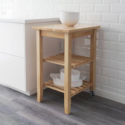 Light wooden kitchen cart with wheels, shelves holding white bowls, against tiled wall.