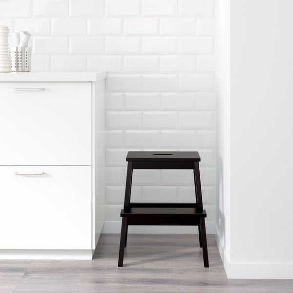 Black wooden stool near white cabinets, aids reaching high items.
