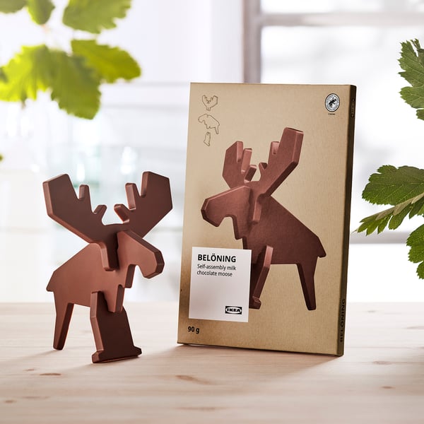 Brown moose-shaped chocolate next to its packaging, placed on a wooden table.