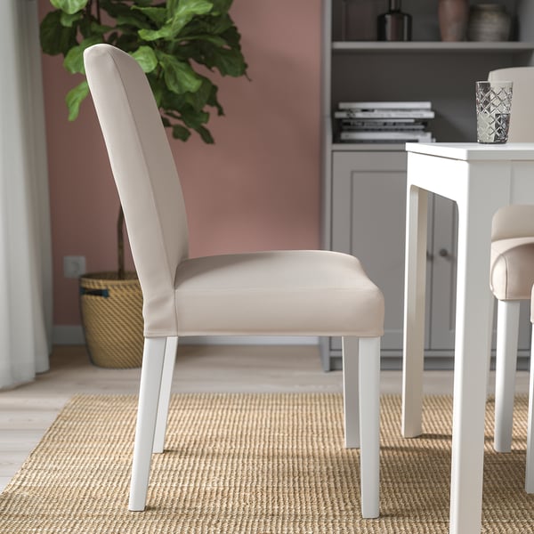 Modern dining chair with beige cover, white legs, atop jute rug near table and plant.
