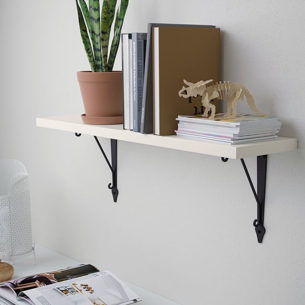 A wall-mounted shelf, holding books, a potted plant, and a dinosaur model, supported by black brackets.