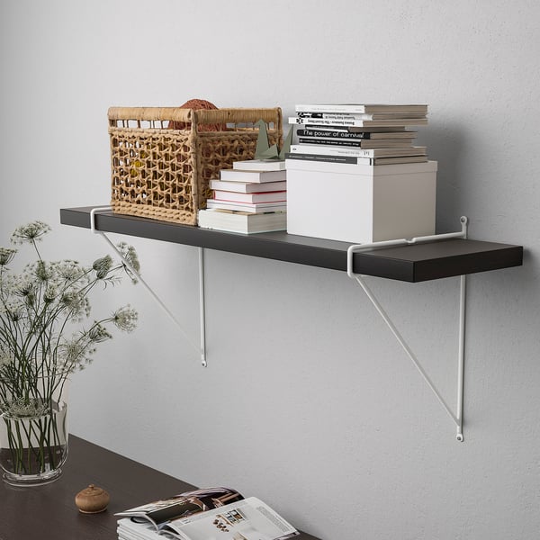 A wall-mounted shelf with black and white brackets holds baskets, books, and a white box. Decorated with dried flowers.