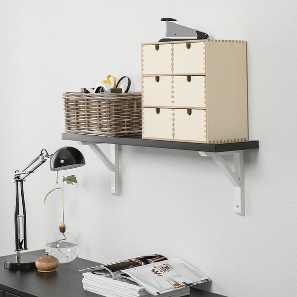 Wall-mounted shelf with wooden doors and a basket holding scissors and glasses, alongside a desk lamp, vase, and magazines on a desk.
