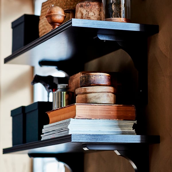 Black shelf with stacked books and wooden boxes. Bevelled and smooth edges. Stylish storage.