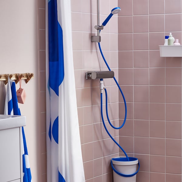 Bathroom with blue BERGVATTNET shower hose diverting water into a grey bucket. Pink tiles and hanging towels.