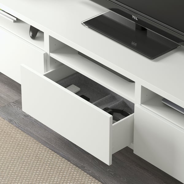 White tv stand with open drawer showing gaming controllers. Tv is on top.