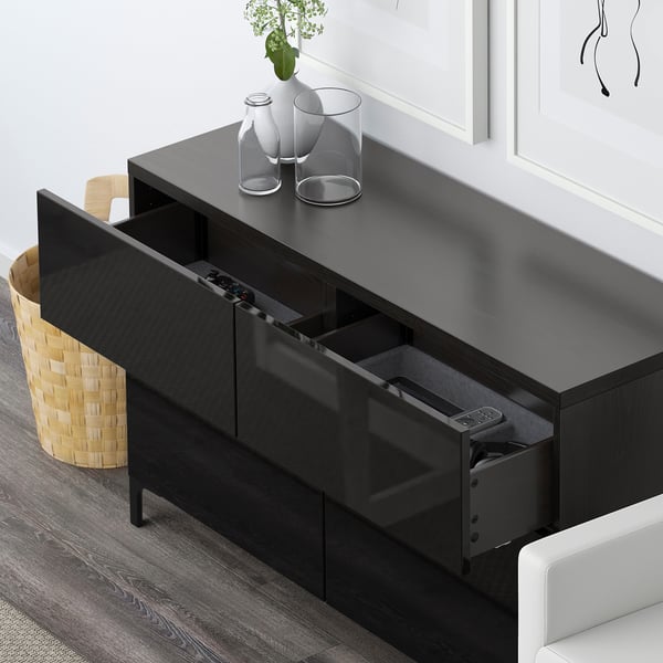 Black BESTÅ media unit with open drawers, remote control, vases, and chair.
