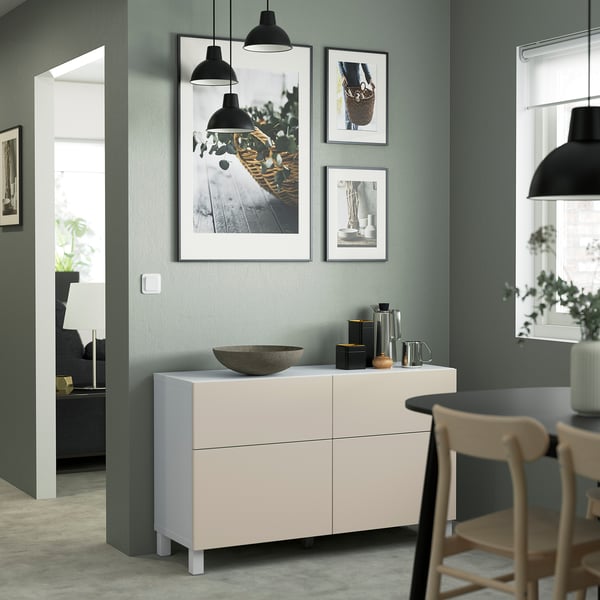 Modern living room with light furniture. White BESTÅ sideboard, photos, pendant light, bowl. Green wall, wooden chair, grey rug, lamp, white door.