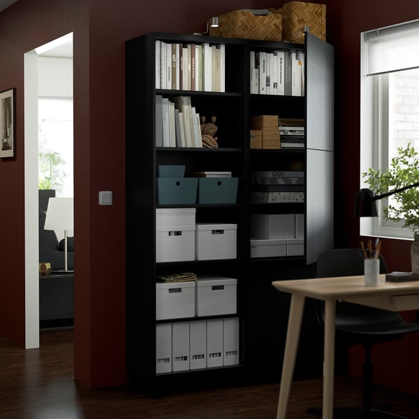 A black BESTÅ storage unit holds books and boxes on shelves, with a push-opener mechanism. Adjustable shelves and hinges optimise storage.