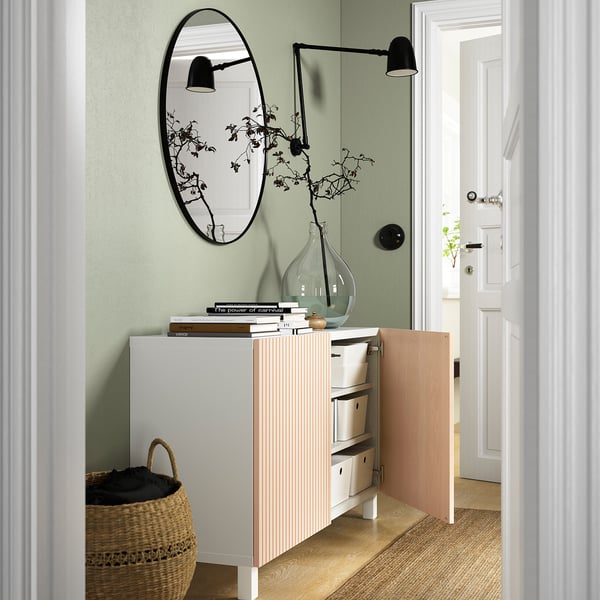 A modern living area a BESTÅ sideboard with adjustable shelves and drawers for storage. An open door reveals organized items inside.