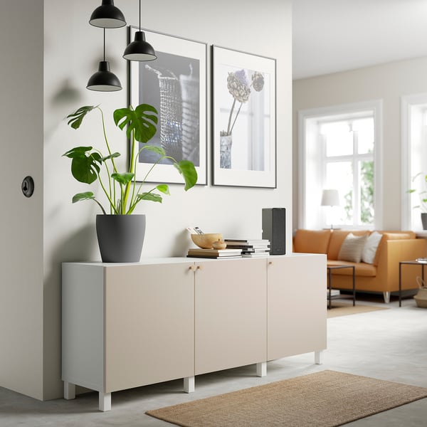 White BESTÅ sideboard with adjustable shelves, holding a large potted plant and framed art. Positioned beside a room with orange sofa and jute rug.