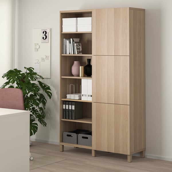 BESTÅ cabinet in light wood with open & closed storage, displaying decor next to a plant and white wall.