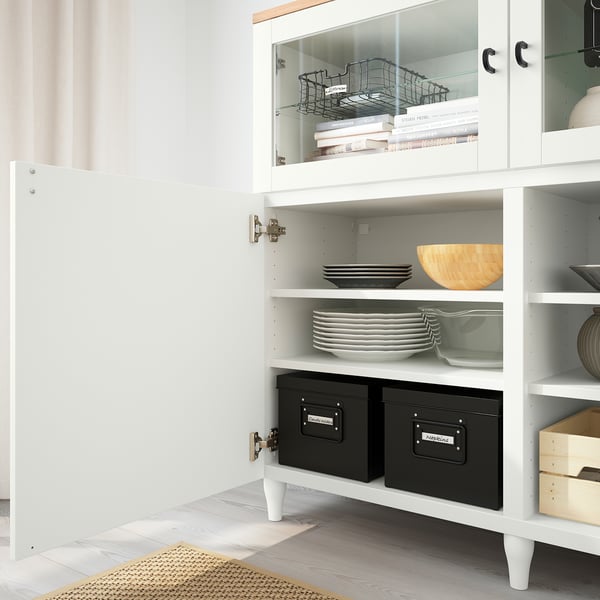 White BESTÅ cabinet with glass doors showing plates, bowls, and boxes. Soft-close drawers and adjustable shelves for neat storage and display.