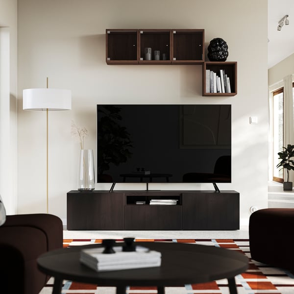 Modern living room with BESTÅ tv bench, flat-screen tv, wall shelves, leather seating, coffee table, books, and lamp.