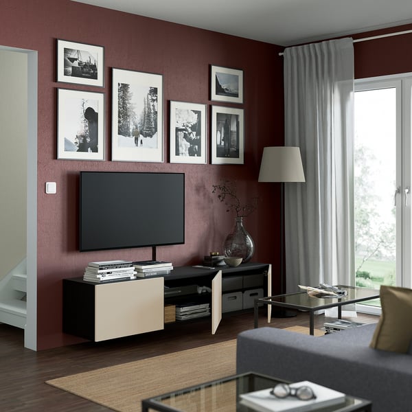 Modern living room with maroon walls, BESTÅ tv bench, books, vase, framed photos, glass coffee table, magazines, grey sofa, large window.