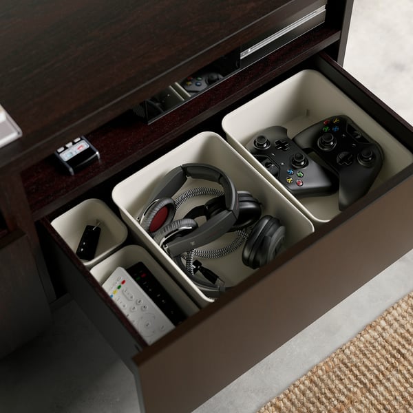 Open brown BESTÅ tv bench reveals drawers for electronics storage. Two gaming controllers and headphones neatly organised in separate compartments.