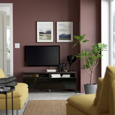Modern living room with maroon walls, black BESTÅ tv unit, framed photos, yellow cushions, and plant.