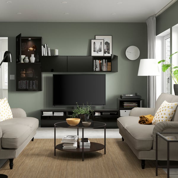 Modern living room with green walls, light-colored couches, and a black tv stand featuring adjustable shelves and cable management.