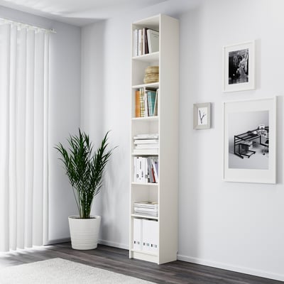 Minimalist corner with white BILLY bookcase, filled with books and plant. Tall, adjustable shelves display items neatly.