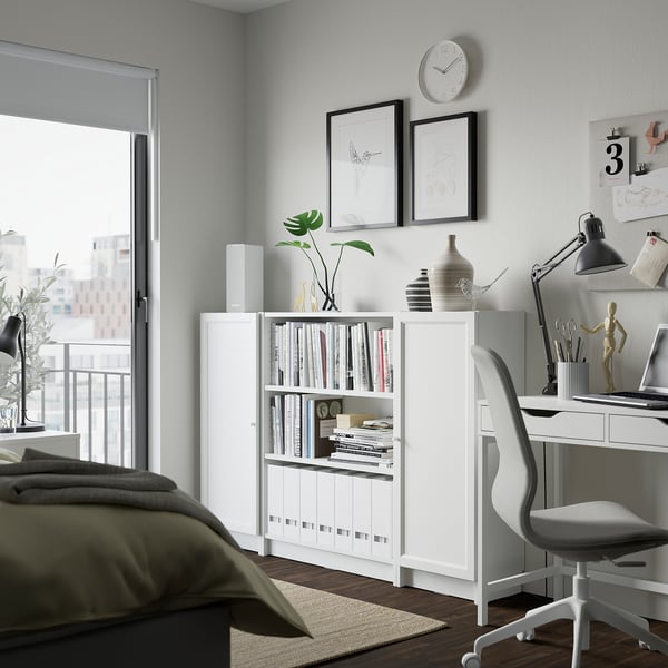 Modern home office featuring white BILLY bookcase with open shelves filled with books and decorative items. Includes desk, white chair, and wall art.