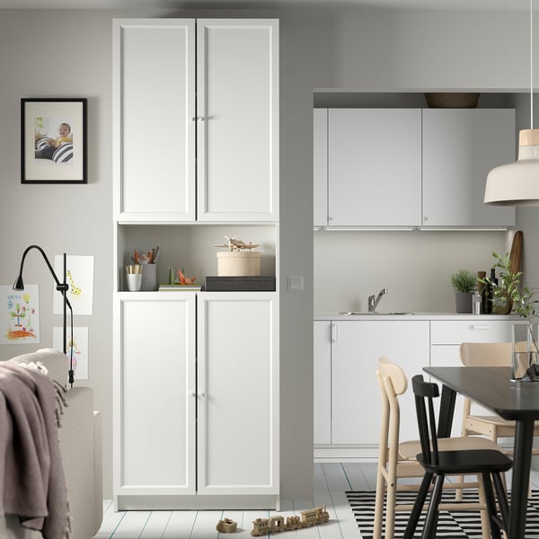 Modern living space with BILLY bookcase, chairs, table, and kitchenette. Bookcase has open and closed storage in white.