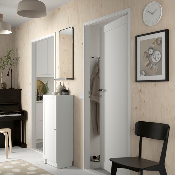 Modern hallway with BILLY white cabinet, mirror, black chair, coat hooks, wall clock, and piano. Light wood walls, minimalist design.