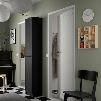 Black BILLY bookcase against green wall near white door, taller than chair, next to clock and wooden shelf.